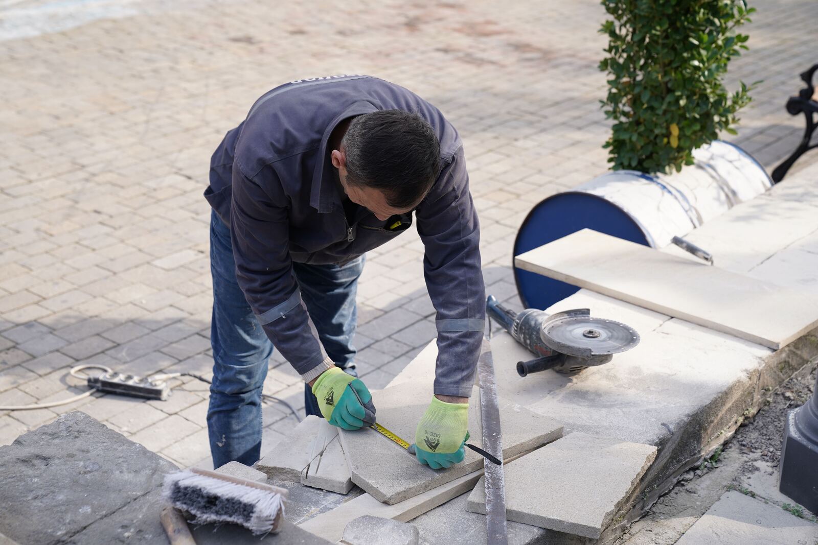 Installer measuring and cutting pavers on a sunny job site